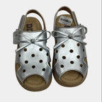 Pair of silver sandals with bow details on a light gray background