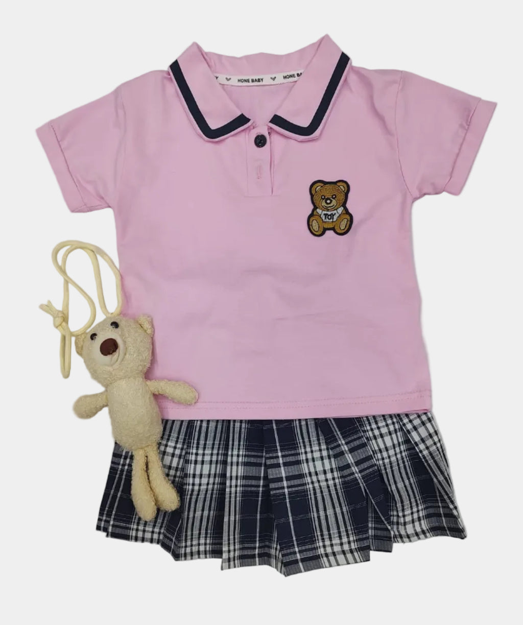 Pink dress with plaid skirt and teddy bear toy on a light gray background