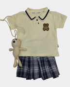 Baby outfit with yellow onesie, blue plaid pants, and stuffed toy on a light gray background