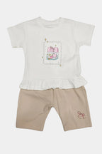 White ruffled top with cartoon design and beige shorts on a light gray background