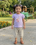 Young girl standing on a path in a park with trees and playground equipment in the background.