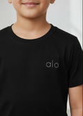 Child wearing a black t-shirt with 'alo' logo on a plain background